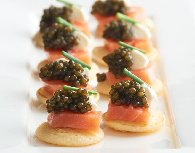 acht Blinis, belegt mit filletiertem Räucherlachs und Kaviar, garniert mit Crème Fraîche und Schnittlauch